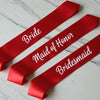 Red sashes with 'Bride', 'Maid of Honor', and 'Bridesmaid' text on a white marble background