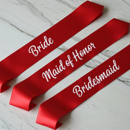 Red sashes with 'Bride', 'Maid of Honor', and 'Bridesmaid' text on a white marble background