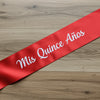Red sash with 'Mis Quince Años' text on a wooden surface