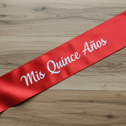 Red sash with 'Mis Quince Años' text on a wooden surface
