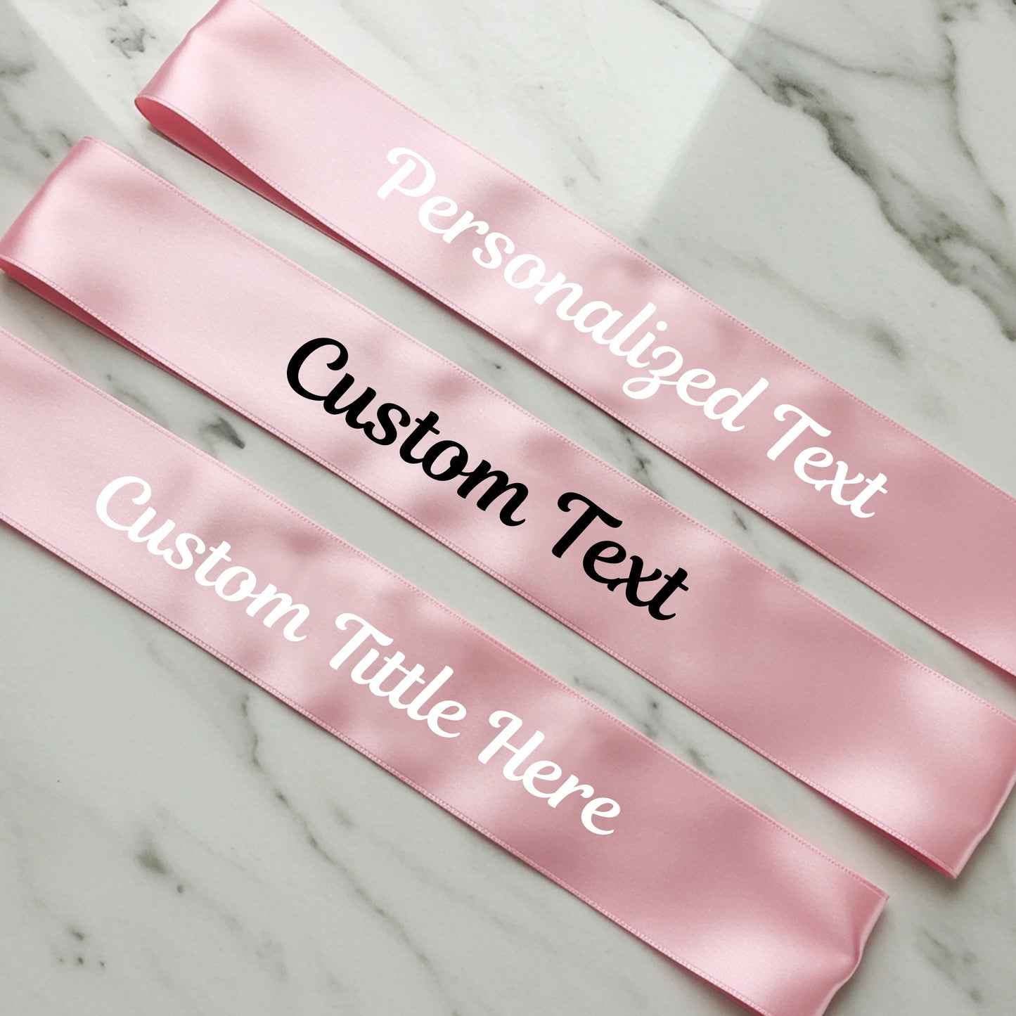 Pink satin sashes with customizable text on a marble surface